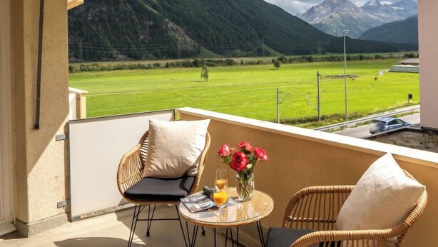 A balcony with wicker chairs and a small table, overlooking a green field and mountains. - Chesa Muntarütsch by Interhome (Samedan)