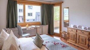A bedroom with a bed, desk, chair, and a dresser. There are curtains on the windows, and a balcony is visible through the glass doors. - Chesa Muntarütsch by Interhome (Samedan)