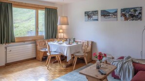 A cozy room with a wooden table and chairs, a window with curtains, a radiator, and a wall with three framed pictures. - Chesa Muntarütsch by Interhome (Samedan)