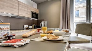 A modern kitchen with a dining table set for breakfast, including croissants, juice, and a coffee machine. - The magnificent residence in the heart of 8th district- rue de la Boetie (Paris)