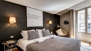 A modern bedroom with a large bed, two bedside tables, a chair, and a view of a building through the window. - The magnificent residence in the heart of 8th district- rue de la Boetie (Paris)