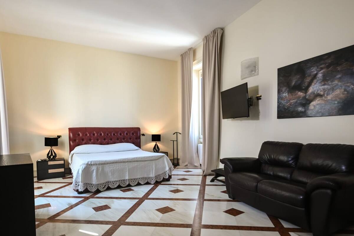 A hotel room with a bed, a leather sofa, a flat-screen TV, and a painting on the wall.