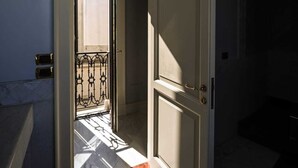An open door leading to a balcony with a metal railing, a tiled floor, and a light switch on the wall. - La putea suite (Lecce)