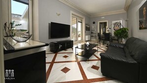 A modern living room with a flat-screen TV, a glass coffee table, a black leather sofa, and a patterned floor. - La putea suite (Lecce)