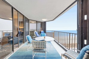 Een balkon met een glazen deur, een ronde tafel en blauwe stoelen.