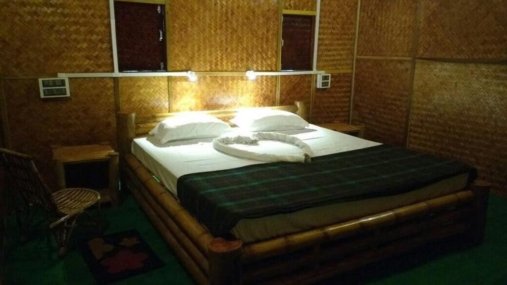 A wooden-framed bed with a green blanket and white pillows, a small bedside table, and a chair.