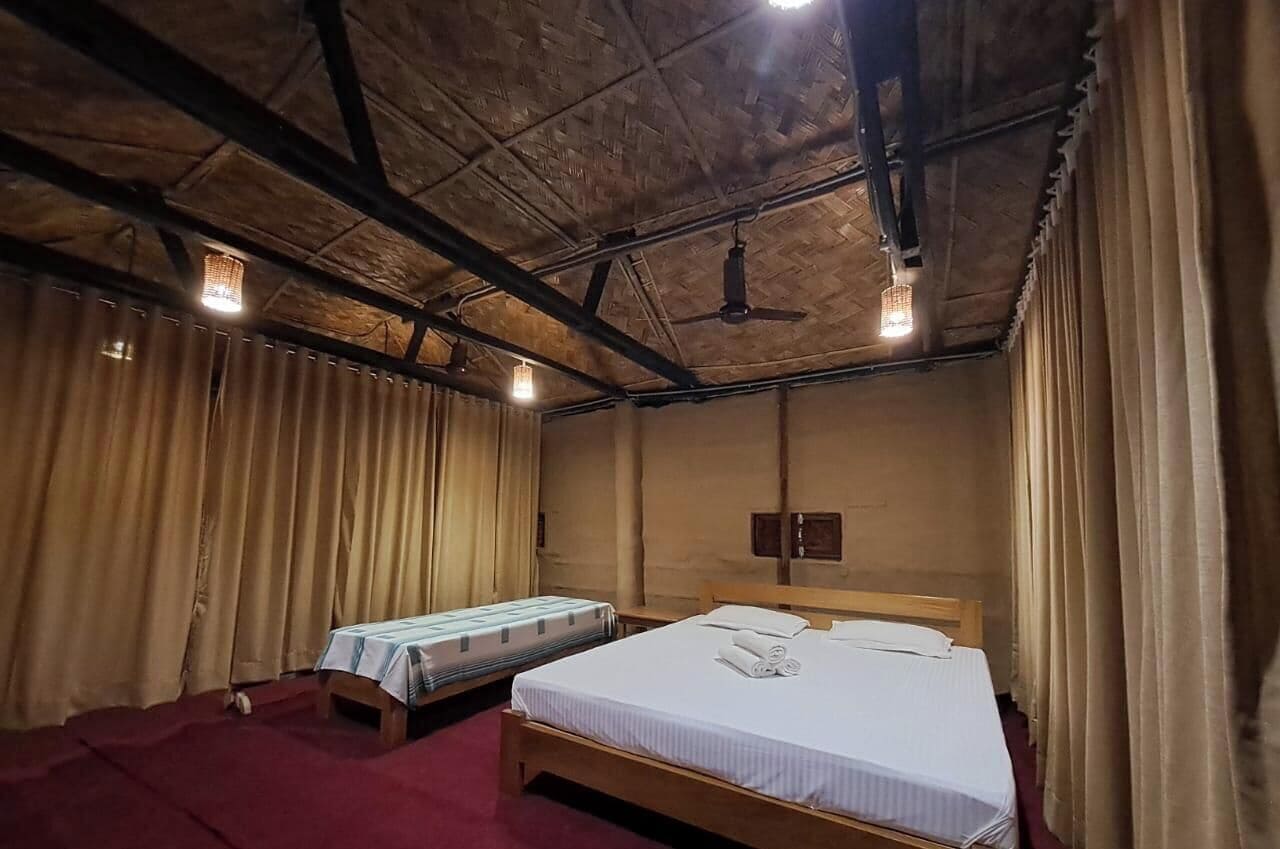 A room with a wooden ceiling, two beds, a wooden headboard, and a red carpet.