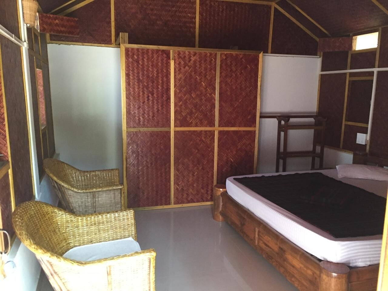 A compact room with a bed, two wicker chairs, a small table, and a whiteboard.