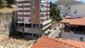 Un edificio residencial de varios pisos con balcones, un área de estacionamiento y un paisaje montañoso al fondo.