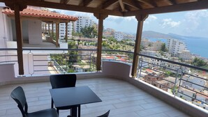 Un balcón con mesa y sillas, con vistas a un paisaje urbano que incluye edificios y el mar.