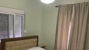 Un dormitorio con cama, cortinas, una ventana con persianas y una lámpara colgante.