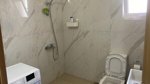 Un baño con ducha, inodoro y un estante pequeño con artículos de aseo.