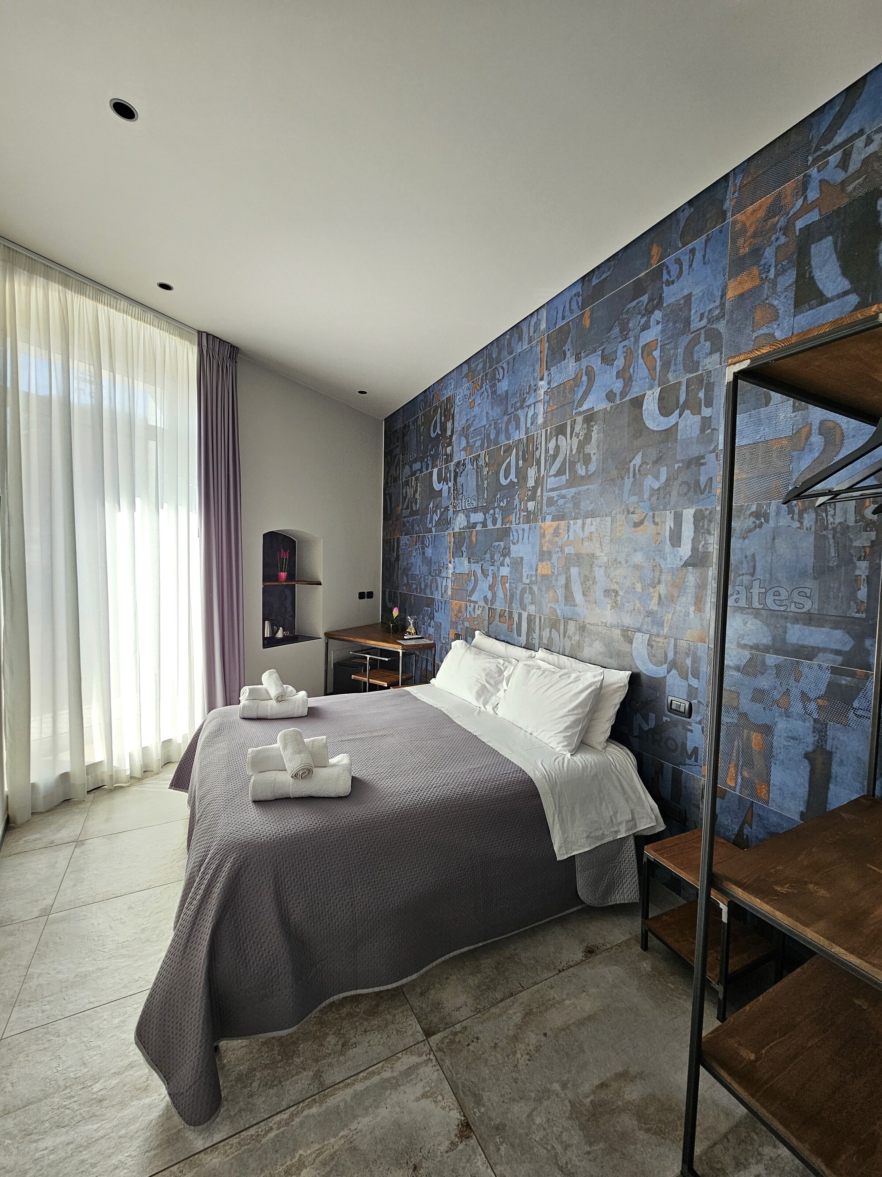 A modern hotel room with a large bed, a desk, and a wall with abstract art.