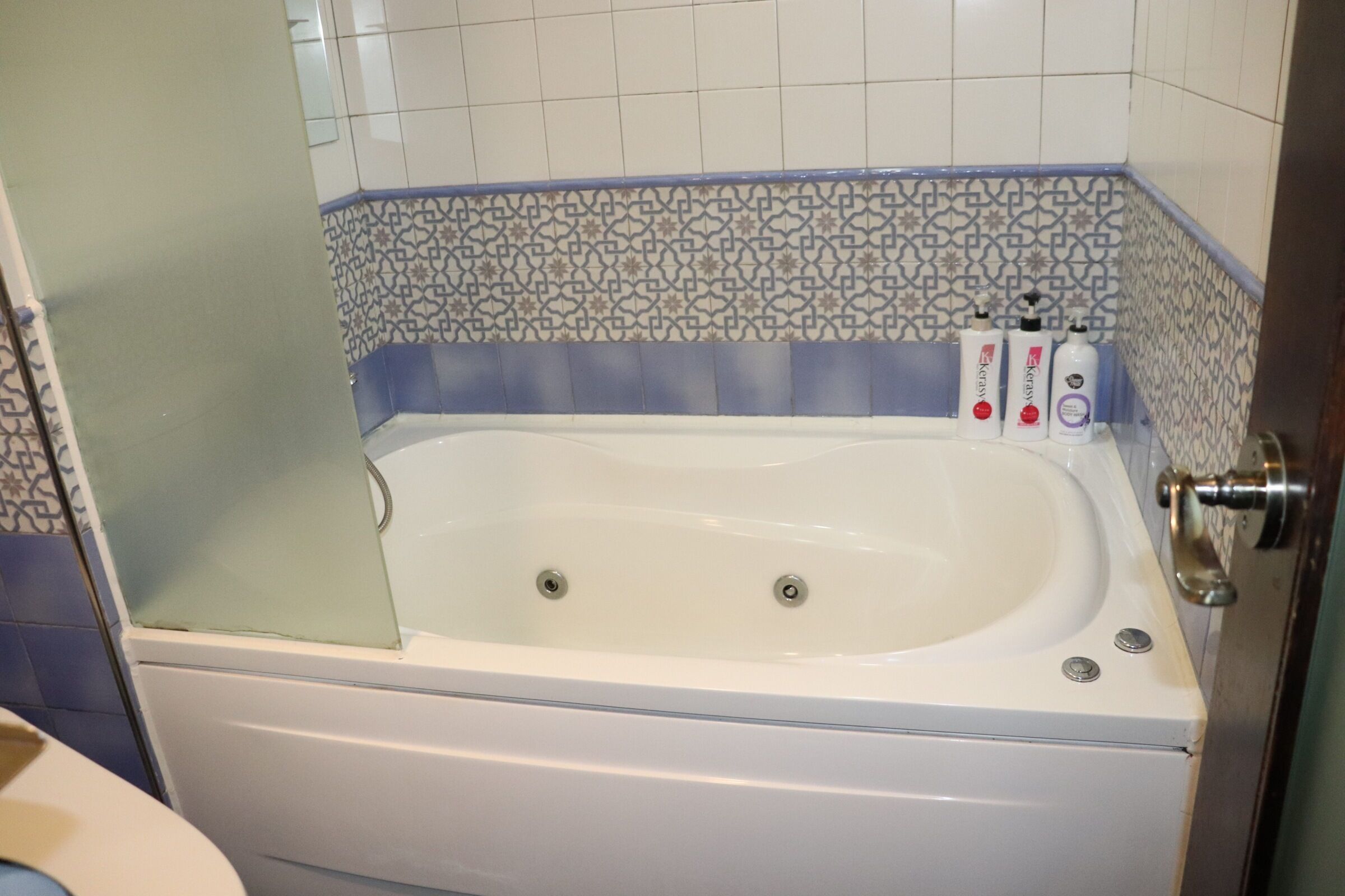 A bathroom with a bathtub, a shower, and a toilet. There are two bottles of shampoo and conditioner on the edge of the bathtub.