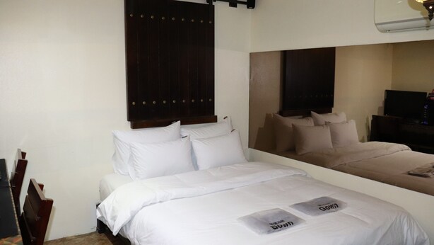 Ein Hotelzimmer mit einem Bett, einem Holzkopfteil, einem Spiegel und einem kleinen Tisch mit einer Lampe.