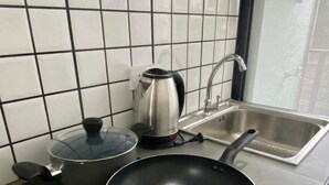 A kitchen with a gas stove, a frying pan, a kettle, and a sink. - Phattharasaya Home (Udon Thani)