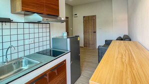 A compact kitchen with a wooden cabinet, a stainless steel sink, and a refrigerator. - Phattharasaya Home (Udon Thani)