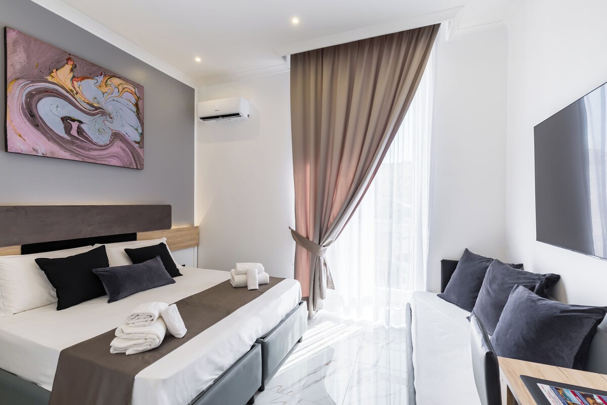 Una camera d'albergo moderna con un letto grande, una scrivania, una TV a schermo piatto e un quadro appeso al muro.
