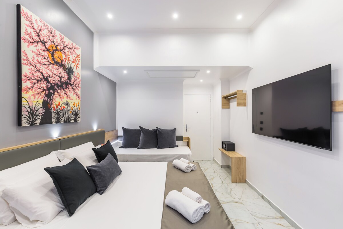 A modern hotel room with two beds, a large TV, and a painting on the wall.