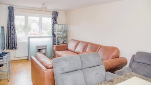 Un salon avec un canapé, une table basse et une cheminée. Il y a une fenêtre avec des rideaux et un radiateur.