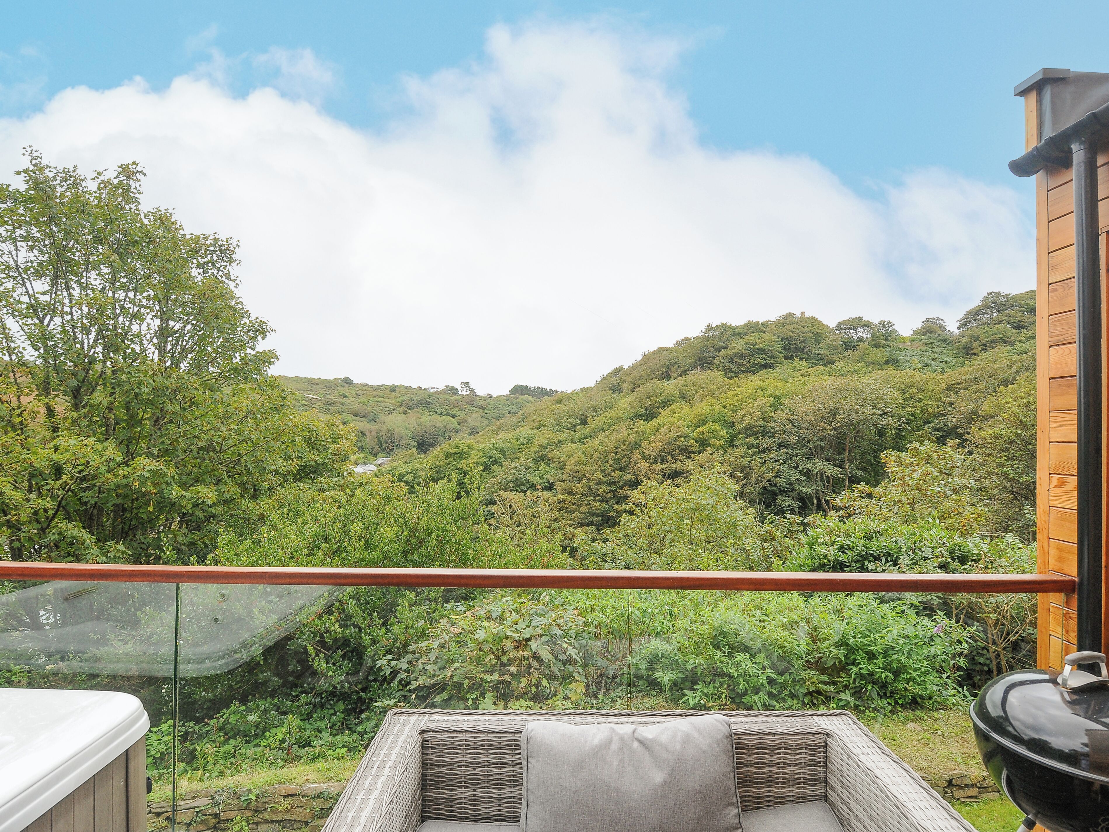 A balcony with wicker furniture, a hot tub, and a view of a lush valley.