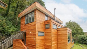 A modern wooden house with a staircase leading to a deck, surrounded by greenery. - 9 Cedars (St. Agnes)