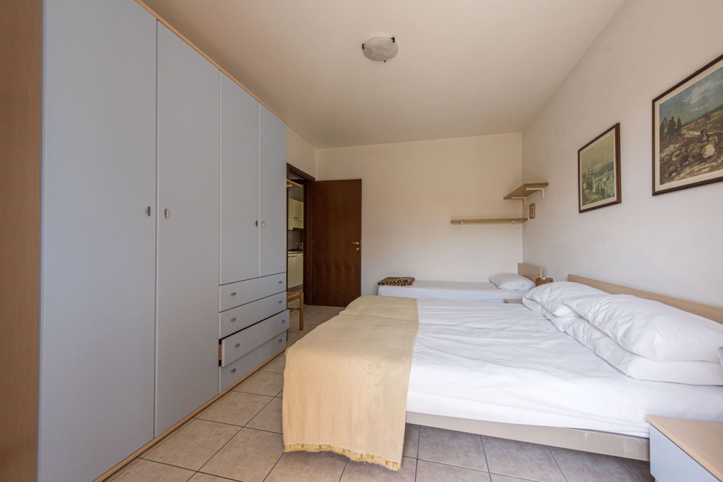 A bedroom with a bed, a wardrobe, a nightstand, and a painting on the wall.
