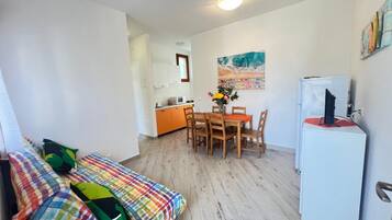 A compact living space with a bed, a dining table with chairs, a small kitchen area, and a refrigerator.