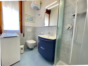 A bathroom with a toilet, sink, shower, and a window with curtains.