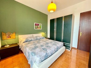 A bedroom with a bed, a nightstand, a lamp, a picture on the wall, and a wardrobe.