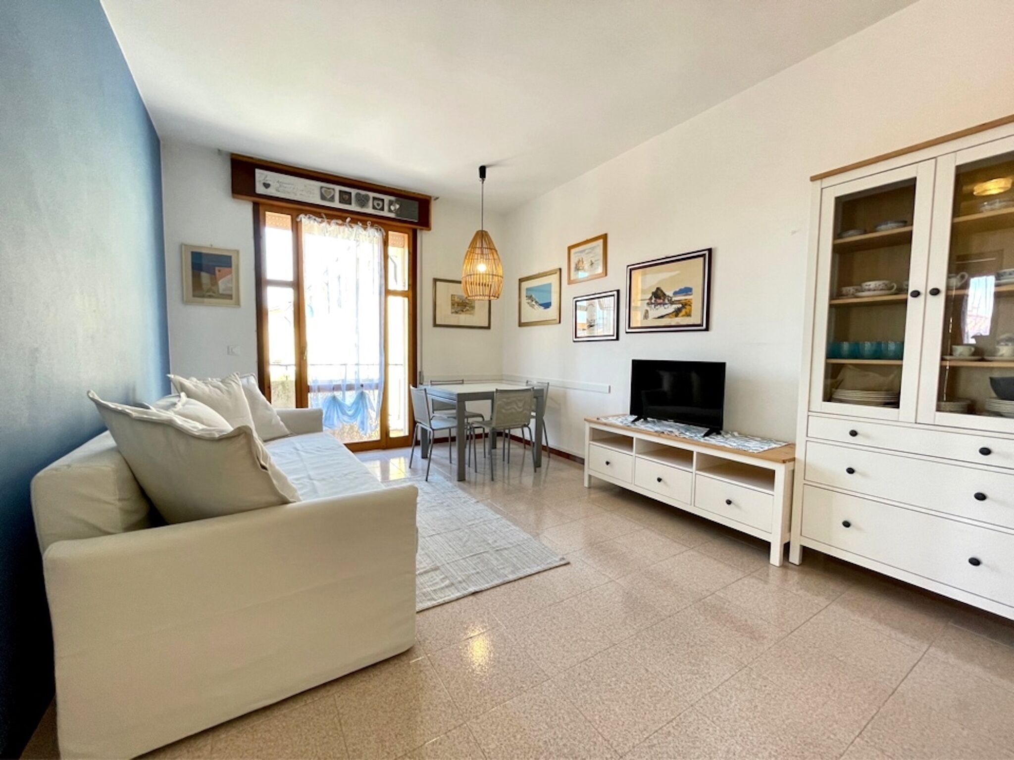 Un salon comprenant un canapé, un téléviseur, une table à manger, des chaises et un meuble avec des portes en verre.