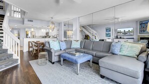 Un salón amplio con un sofá seccional gris, una mesa de centro y una escalera que lleva a un nivel superior.