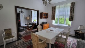 A dining area with a table, chairs, a chandelier, a window with curtains, and a view of greenery outside. - Spacious vacation home on 19 hectares of woodland in a secluded location (Gerdau)