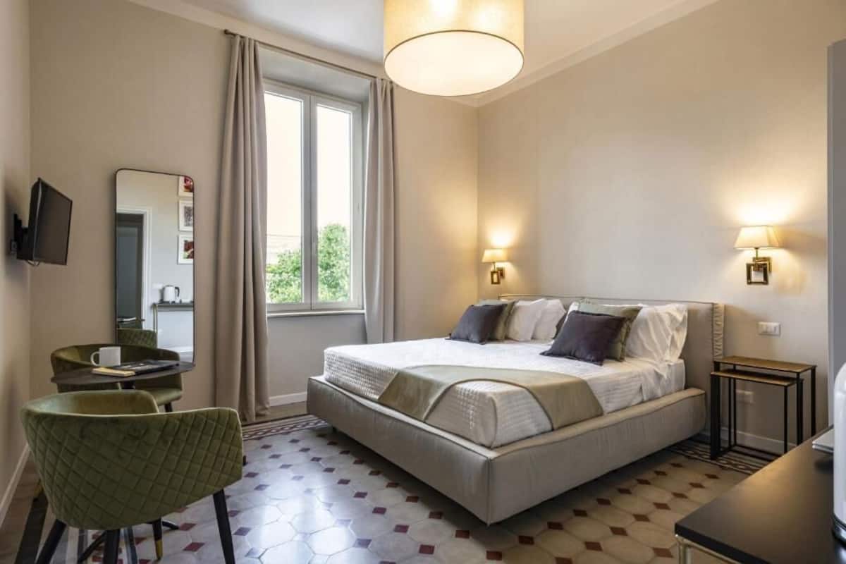 Una habitación de hotel con cama, escritorio, silla, televisión y ventana con cortinas.