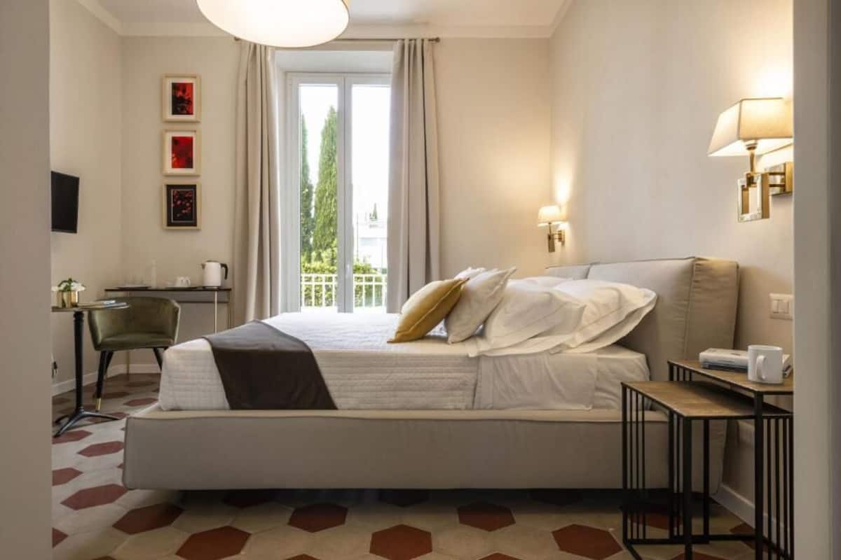 Habitación de hotel con cama, escritorio, silla, lámpara y vistas al exterior.