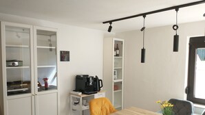 Ett kompakt kök med en kaffemaskin, ett matbord med en vas med blommor och en stol.