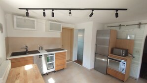 Ett modernt kök med ett kylskåp i rostfritt stål, en mikrovågsugn och en diskmaskin. Det finns ett träbord och en diskho med blandare.