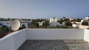Una terraza en la azotea con suelo estampado, una antena parabólica y vistas de edificios circundantes.