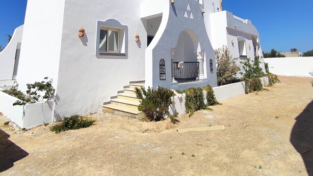 Un edificio blanco con un arco de entrada destacado, una escalera que conduce a la puerta y un cielo azul claro al fondo.