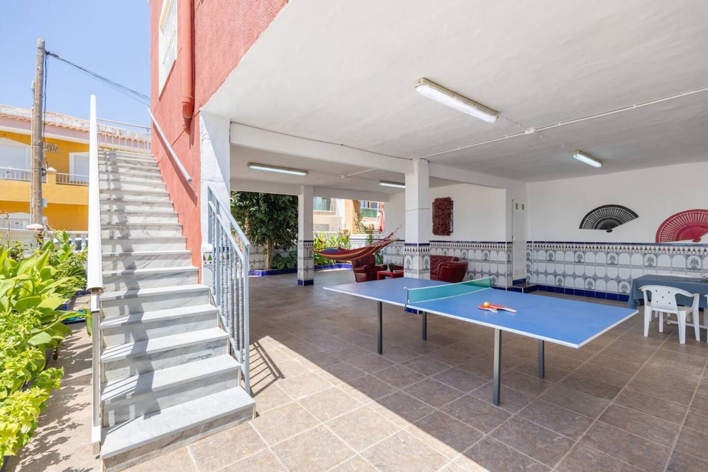 Un espace extérieur aménagé en terrasse, avec une table de ping-pong, un hamac et un escalier menant à un niveau supérieur.