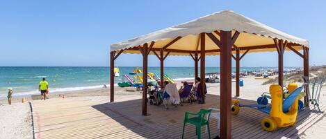 A beach with a wooden deck, a covered seating area, and beach equipment.