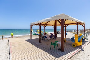 Ein Strand mit einer Holzterrasse, einer überdachten Sitzgelegenheit und Strandausstattung.