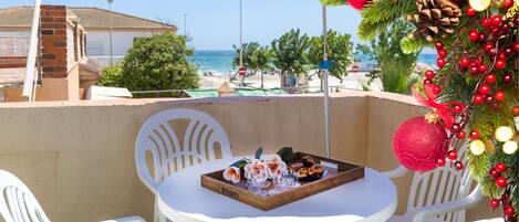 A terrace with a table set for two, overlooking a beach and a building.