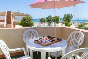 Ein Balkon mit Tisch für zwei Personen, einem pinken Sonnenschirm und Blick auf den Strand.