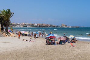 Ein Strand mit badenden Personen, Sonnenschirmen und blauem Himmel.