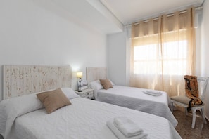 Ein Hotelzimmer mit zwei Betten, einem Nachttisch mit Lampe, einem Sessel und einem Fenster mit Vorhängen.