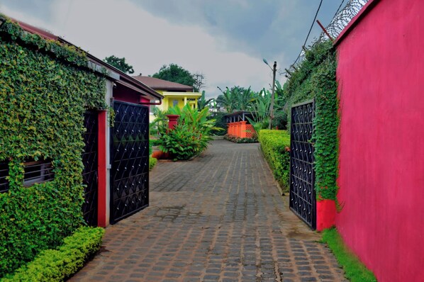 A narrow cobblestone alleyway flanked by buildings with black gates and lush greenery.