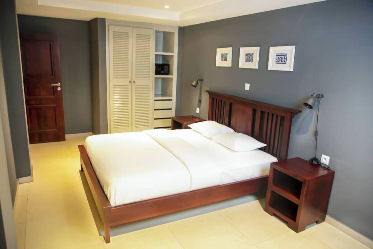 A bedroom with a wooden bed, a nightstand, a wardrobe, and a desk with a lamp.