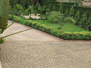 A paved courtyard with a stone pathway, surrounded by lush greenery and a variety of plants. - Riad Prince Louis (Yaoundé)