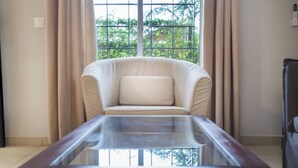 Una habitación con una mesa de vidrio, un sofá color crema y vistas a la vegetación a través de amplias ventanas.